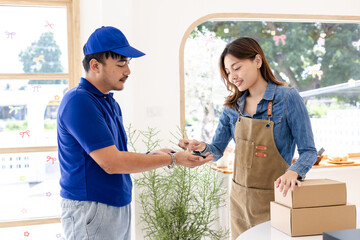 Courier and female small business entrepreneur verifying package via smartphone in coffee shop, shipping package cashless payment, professional delivery service, technology online orders fast services