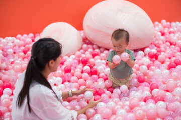Happy mum enjoying playful moment with son in pink ball pit