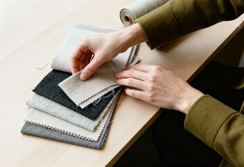 A designer's hands choosing from a collection of neutral fabric swatches. Tailor selecting textile samples for a creative project in a workshop
