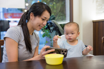 Mother feeding baby while baby looking at phone