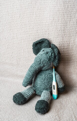 Toy elephant with thermometer lays covered with baby blanket- top view. Children Healthcare concept photo.
