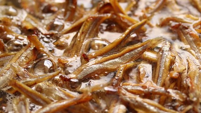 Fried small dried anchovies fish in the boiling oil. Close-up view
