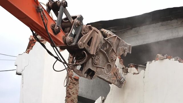 Excavator is actively breaking down the wall of a building, demonstrating the powerful machinery used in construction and demolition projects.