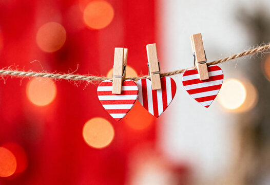 Three decorative striped hearts pinned to a string, set against a bright red background with bokeh circles