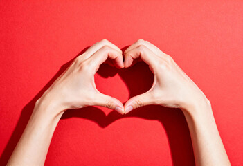Pair of hands making heart gesture with shadow on vibrant red background for Valentines Day or mothers day
