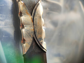 Close-up of a dark metal flat bar or blade secured by a unique, light-colored, patterned metal clamp or handle piece, highlighting industrial tool design, texture, and abstract mechanical detail.