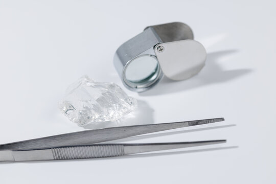 Jeweler's loupe, raw gemstone, and tweezers on white background