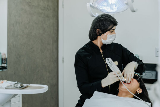 Dental assistant scanning patient&rsquo;s teeth with digital intraoral scanner inside modern dental clinic setup.