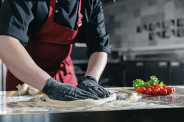 Chef preparing pizza dough in professional pizzeria kitchen tomatoes and mushrooms, dark light