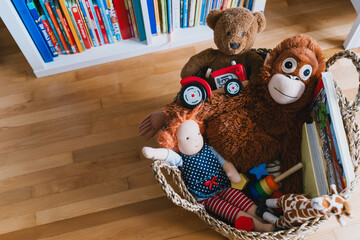 Interior decor of children's room with basket full of toys and book corner of child's literature. Organizing storage in kids room: bookshelves and educational and soft toys. Montessori education.