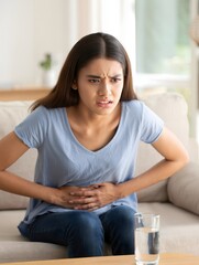 Woman Experiencing Stomach Pain on Sofa with Glass of Water Nearby