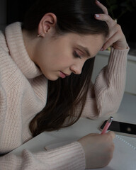 Young woman writing notes at desk in cozy sweater