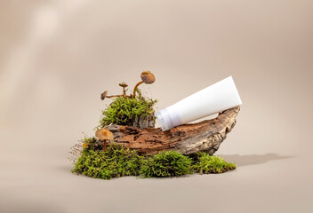 a white cosmetic tube on the podium made of tree bark next to moss and mushrooms . The concept of a cream with natural ingredients.