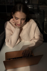 A young woman working on a laptop with a thoughtful expression, indoor lifestyle photography