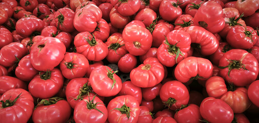 Heap of ripe pink tomatoes scattered on market stall, rustic harvest scene highlighting fresh...