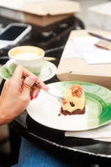 Hand Holding Spoon Over Gourmet Dessert on Green Ceramic Plate in Café Setting