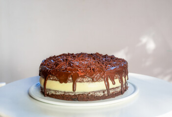 Chocolate carrot cake with cream cheese frosting, topped with chocolate ganache and sprinkled with shredded chocolate, placed on a white ceramic plate.
