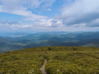 Sweeping sky filled with layered clouds above gentle green mountain ridge and distant blue hills.