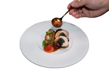 A close-up shot of a gourmet dish being expertly plated and sauced. A chef's hand delicately garnishes the meal with sauce