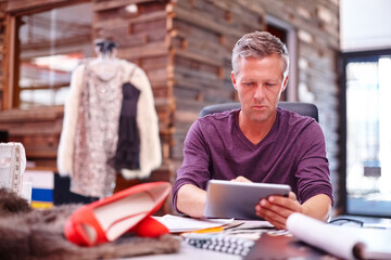 Fashion designer, mature man or tablet in workshop for creative project, trend research or planning. Clothing production, owner or digital app in studio for design process or sourcing material online