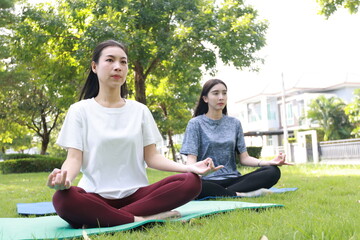 Asian woman practicing yoga out door in the garden with her friend. Two women relaxing after wprkout.