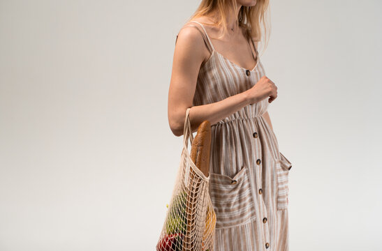 Minimal portrait of woman in striped dress with reusable eco mesh bag full of groceries
