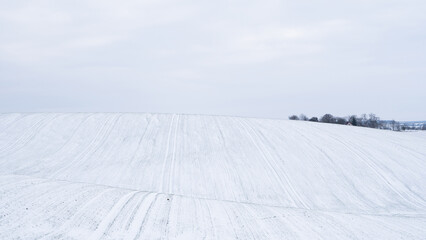 Snow-covered agricultural hills under cloudy winter sky in rural landscape