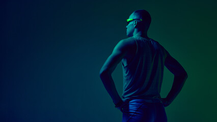 Athlete standing hands on hips in blue-green neon studio lighting. Concept of sports motivation visuals, trainer profile design, fitness challenge promos, athleticwear showcases.