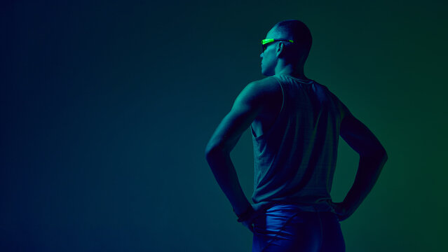 Athlete standing hands on hips in blue-green neon studio lighting. Concept of sports motivation visuals, trainer profile design, fitness challenge promos, athleticwear showcases.
