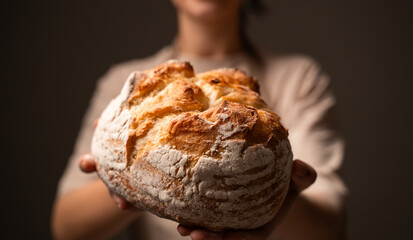 Baker presenting rustic sourdough loaf with golden crust in soft studio light