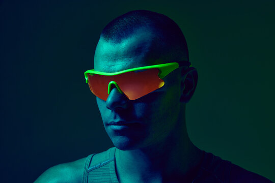 Close-up of athlete wearing neon sports glasses in colored light. Concept of eyewear marketing, sports gear product shots, athlete branding visuals, modern fitness design. - Powered by Adobe
