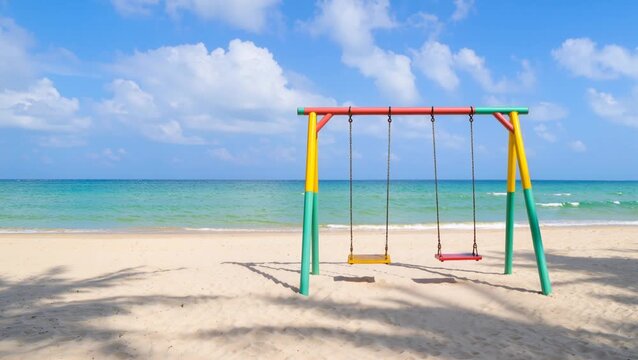 Empty colorful swingset on a sunny beach overlooking the calm blue ocean