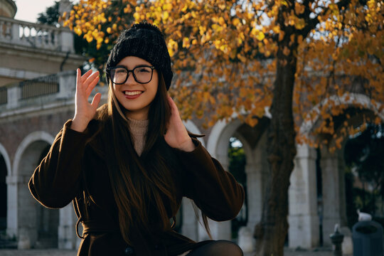 Mujer joven prob&aacute;ndose o ajust&aacute;ndose gafas de ver en un parque urbano.