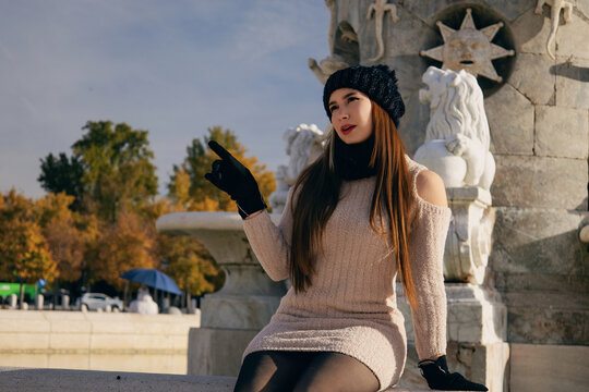 Mujer joven con gorro y bufanda de invierno posando casualmente en parque urbano soleado.