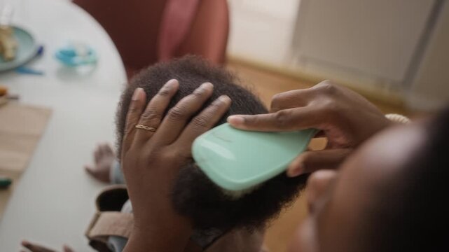 High angle view of African American woman taking off scrunchie and brushing her toddler daughter hair
