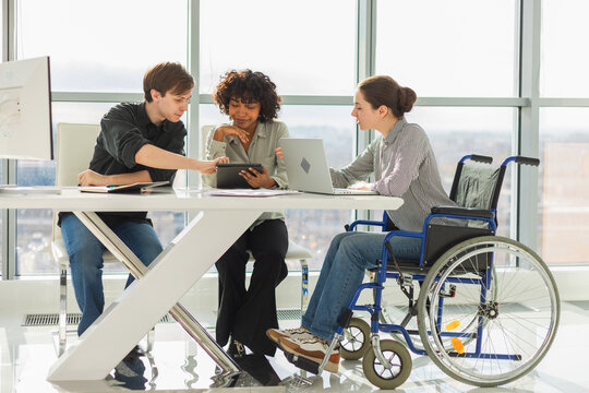 Teamwork brainstorm. Diverse multiracial colleagues woman in chair for people with disability working together. Group of people sitting in creative office discussing business. Young professional team