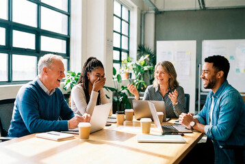 Grupo diverso de compañeros de trabajo riendo y colaborando durante una reunión creativa en una oficina moderna con luz natural.