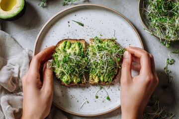 Foods styling magazine content concept. Fresh avocado toast topped with sprouts, held by hands, on a neutral plate.