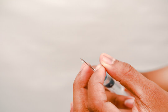 Close-up of a hand holding a syringe with a drop at the needle tip medical shot - Powered by Adobe