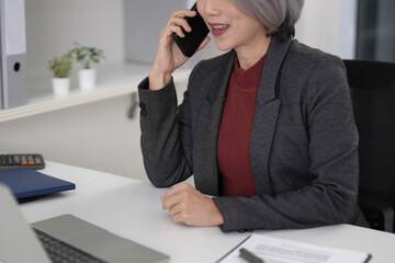 Older Asian businesswoman professional communication business operations modern office desk smartphone conversation client call meeting planning success strategy