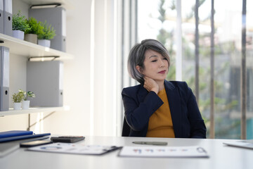 Asian senior business woman neck pain discomfort from office work professional health stress modern workplace environment long hours fatigue