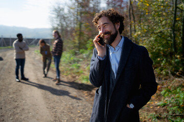 Happy man talking on phone with friends in a forest during a sunny day in autumn