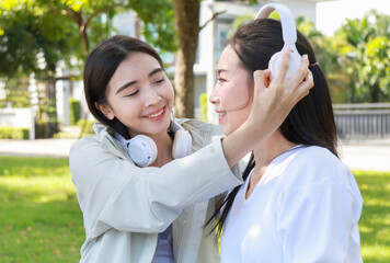 Pretty cheerful asian woman in casual clothes browses laptop computer connected to 4g internet updates software uses modern technologies poses outdoor looks gladfully away with her friend. 