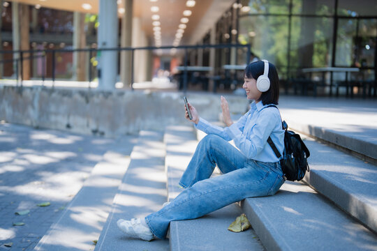 Young student making video call on campus stairs