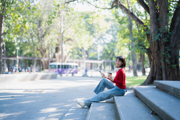 Young Asian student using digital tablet and drinking coffee