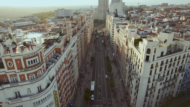 Aerial drone footage flying down the iconic Gran V&iacute;a in Madrid, Spain during a spectacular golden hour sunset, capturing the vibrant city life and traffic below.