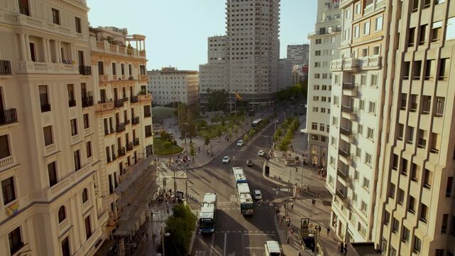 Aerial drone footage flying down a busy street in central Madrid, Spain, towards Plaza de Espa&ntilde;a, capturing city traffic and pedestrians during a beautiful sunset.