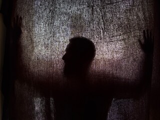 Silhouette of a person behind a dark fabric, mysterious and suggestive atmosphere, thanks to the strong backlighting that emphasizes the silhouette and the irregular texture of the fabric that creates