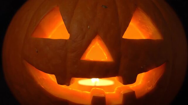 A carved pumpkin with triangle eyes and mouth illuminated by a candle inside
