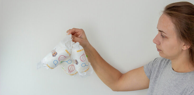 A woman's hand holding two disposable baby diapers against a light background